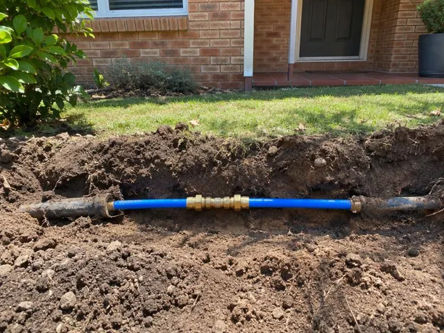 Repaired blue water pipe in a dug trench beside a brick house wall in Brookvale