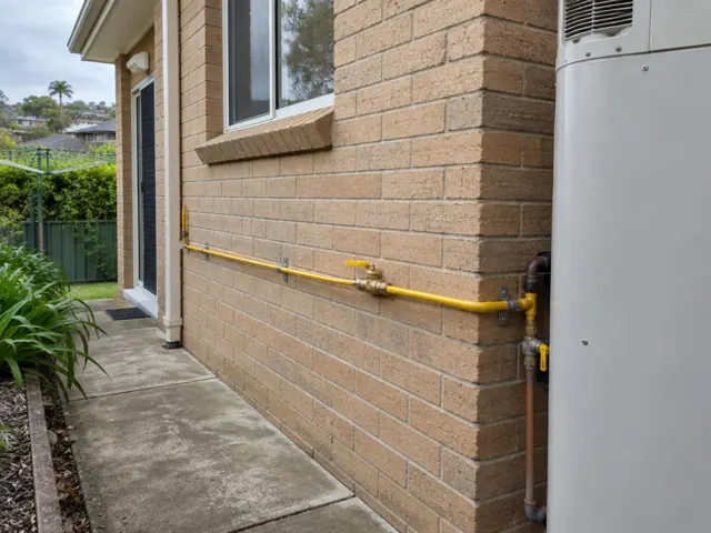 Yellow gas pipe and fittings on a brick exterior wall beside a home unit in Curl Curl
