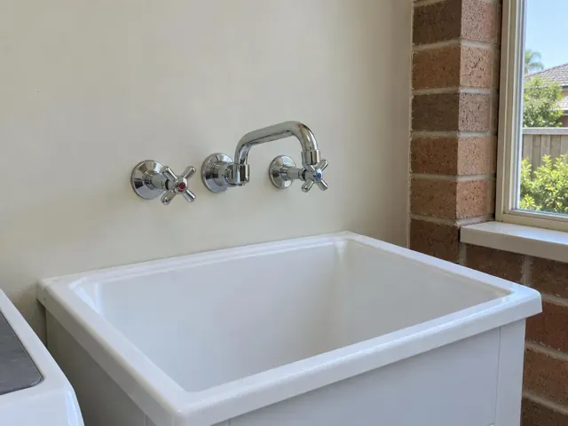 White laundry tub with new wall-mounted taps and spout beside a brick wall and window in Curl Curl